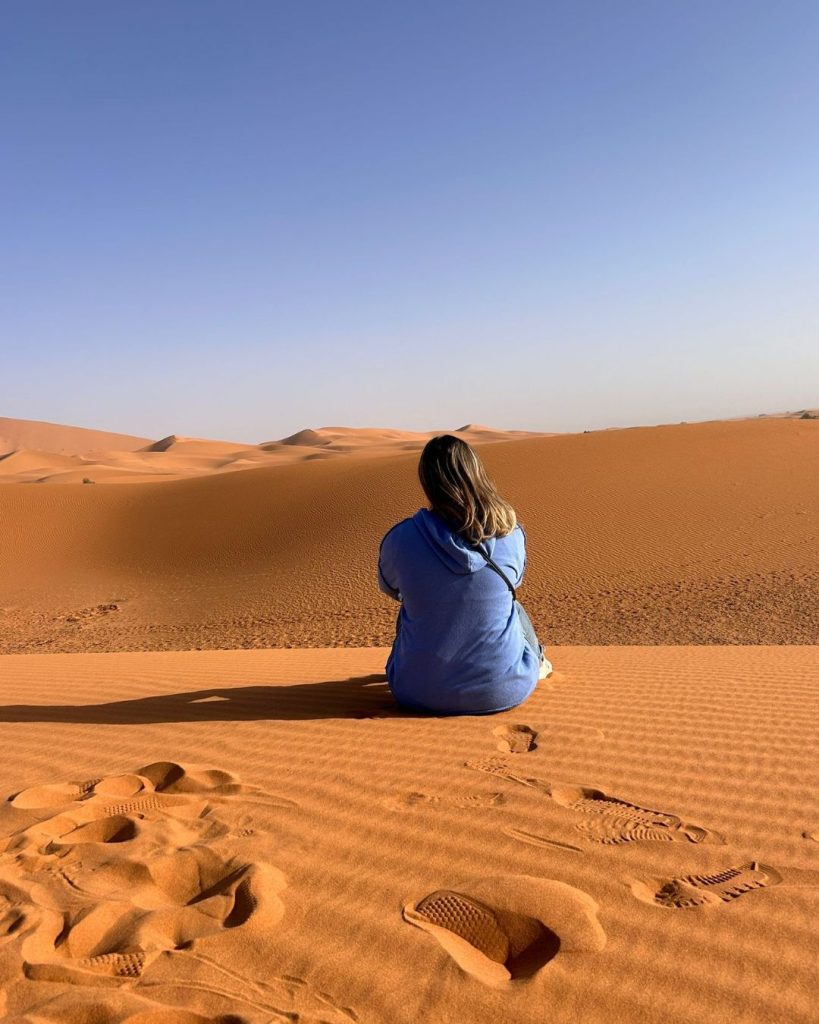 mujer sentada en las dunas del desierto de marruecos mirando el paisaje